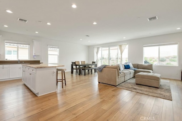 living area with baseboards, light wood-type flooring, visible vents, and recessed lighting