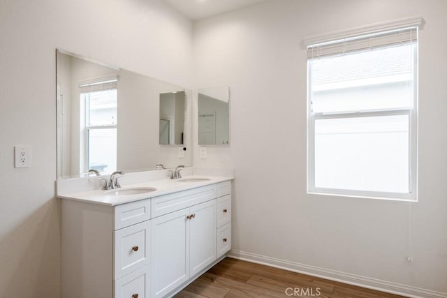 full bathroom with double vanity, a sink, baseboards, and wood finished floors