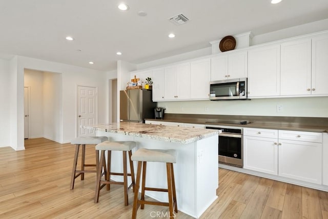 kitchen featuring light wood finished floors, visible vents, a kitchen island, stainless steel appliances, and a kitchen bar