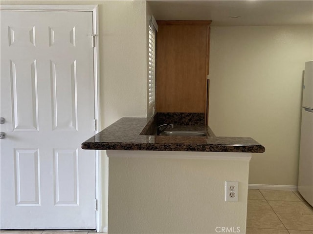 kitchen with dark countertops, light tile patterned flooring, a sink, and baseboards