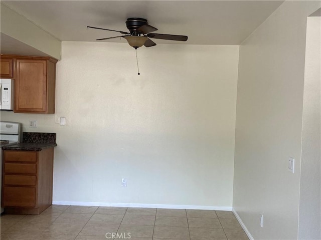 interior space featuring white microwave, brown cabinetry, a ceiling fan, range, and baseboards