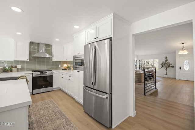 kitchen with light wood finished floors, appliances with stainless steel finishes, wall chimney range hood, and white cabinets