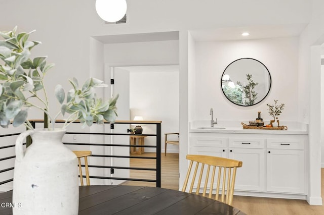 interior space with baseboards, light wood-style flooring, wet bar, a sink, and recessed lighting