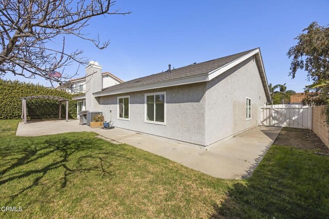 rear view of property with fence, a lawn, stucco siding, a pergola, and a patio area