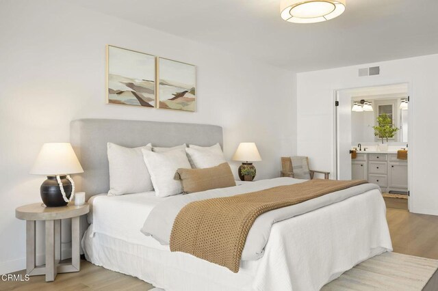 bedroom with light wood-style flooring, connected bathroom, visible vents, and baseboards