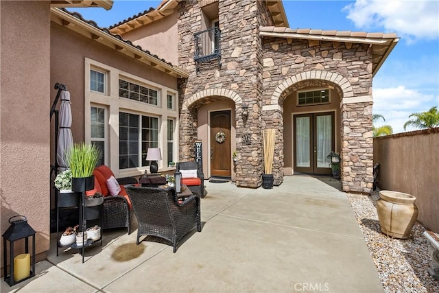 view of patio with a balcony, fence, and french doors