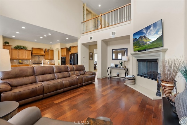 living room featuring a glass covered fireplace, dark wood finished floors, visible vents, and recessed lighting