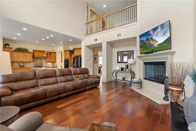 8072 Soft Winds Dr, Corona, CA 92883 - living room featuring dark wood-type flooring, recessed lighting, a glass covered fireplace, and a towering ceiling