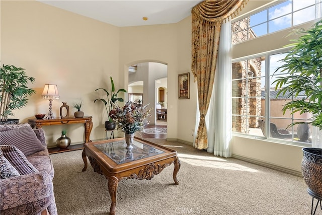 sitting room featuring a towering ceiling, carpet, arched walkways, and a wealth of natural light