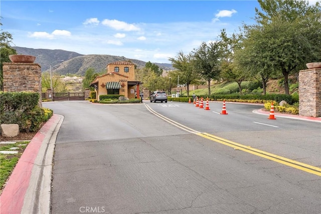 view of road featuring a gated entry, a mountain view, and curbs