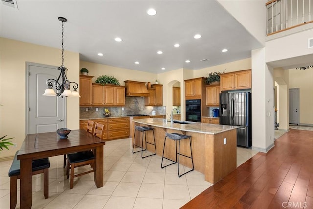 8072 Soft Winds Dr, Corona, CA 92883 - kitchen featuring appliances with stainless steel finishes, custom range hood, arched walkways, brown cabinets, and a kitchen island with sink
