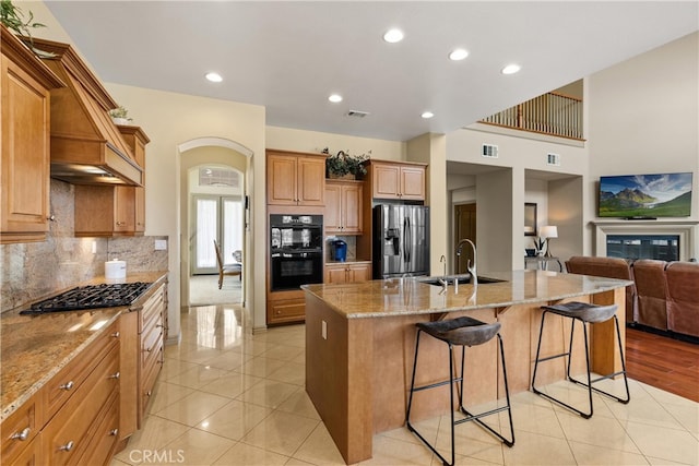 kitchen with dobule oven black, a sink, visible vents, stainless steel refrigerator with ice dispenser, and a kitchen bar