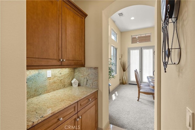 kitchen with light stone counters, arched walkways, visible vents, decorative backsplash, and light carpet