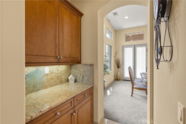 8072 Soft Winds Dr, Corona, CA 92883 - kitchen featuring arched walkways, light stone counters, backsplash, brown cabinets, and recessed lighting