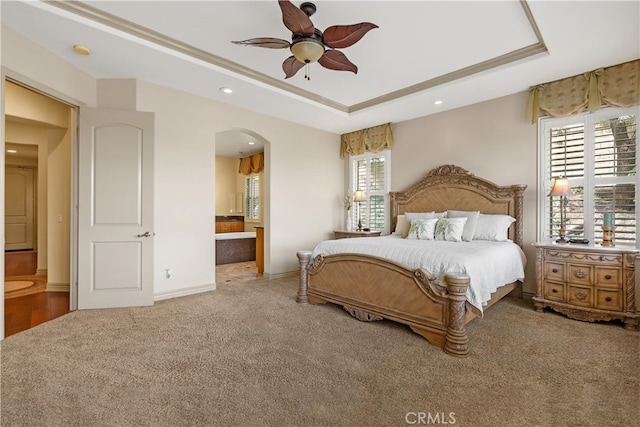 bedroom featuring arched walkways, carpet, a raised ceiling, connected bathroom, and baseboards