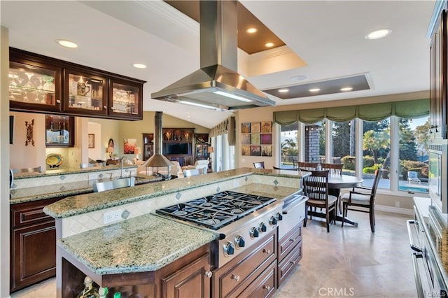 kitchen with glass insert cabinets, a center island, light stone countertops, island exhaust hood, and stainless steel gas stovetop