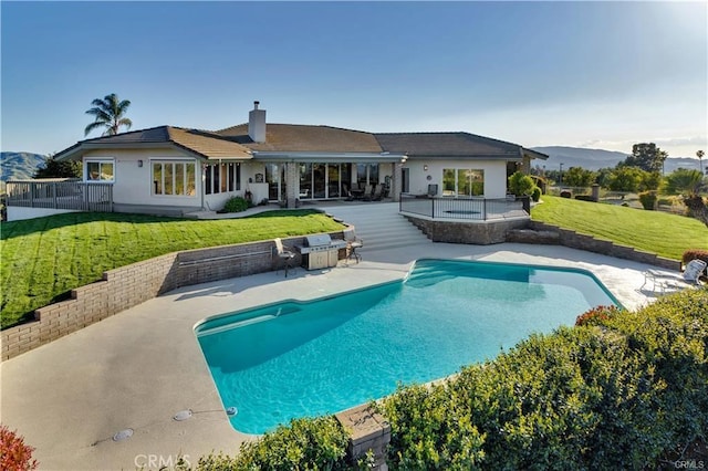 back of house with a yard, a chimney, a patio area, a mountain view, and an outdoor pool