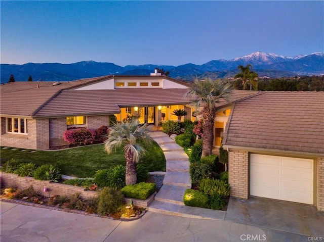 view of front of property with concrete driveway, brick siding, a mountain view, and a front lawn