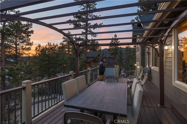 deck at dusk featuring outdoor dining space and a pergola