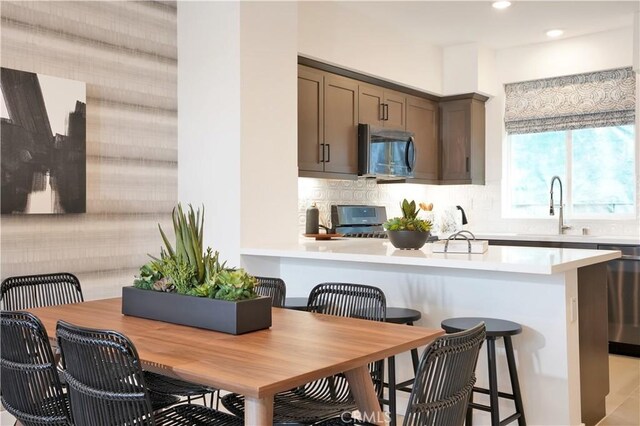 kitchen featuring a breakfast bar area, a sink, light countertops, appliances with stainless steel finishes, and decorative backsplash