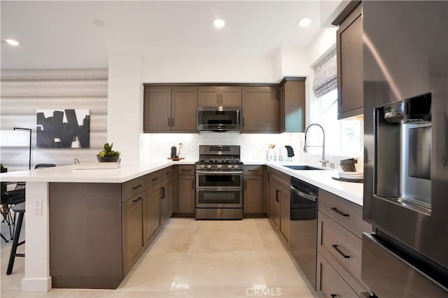 kitchen with tasteful backsplash, appliances with stainless steel finishes, a peninsula, a kitchen bar, and a sink