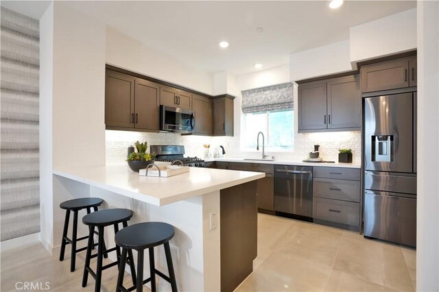 kitchen with a breakfast bar area, a peninsula, stainless steel appliances, dark brown cabinets, and a sink