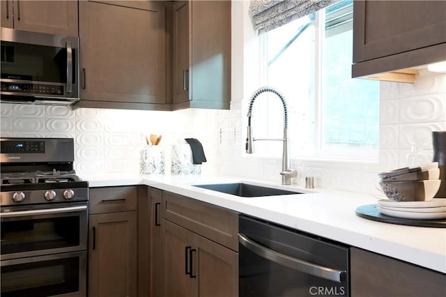 kitchen featuring light countertops, appliances with stainless steel finishes, a sink, and decorative backsplash