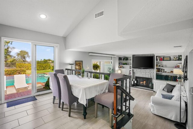 dining area featuring light wood finished floors, visible vents, lofted ceiling, a brick fireplace, and built in shelves