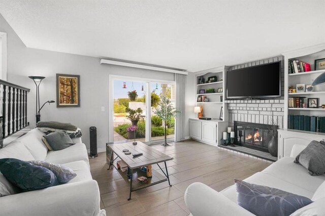 living area featuring light wood-style floors, a large fireplace, built in features, and baseboards