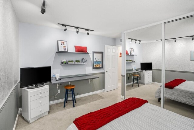 bedroom with a closet, baseboards, light carpet, and track lighting