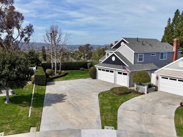 view of front facade featuring a garage, concrete driveway, roof with shingles, a chimney, and a front yard