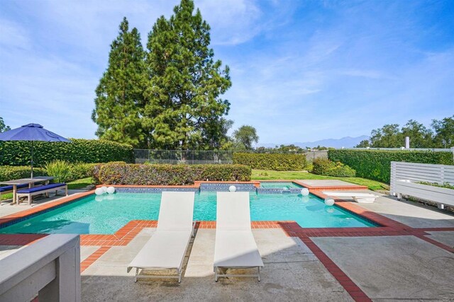 view of pool with a diving board, fence, and a hot tub