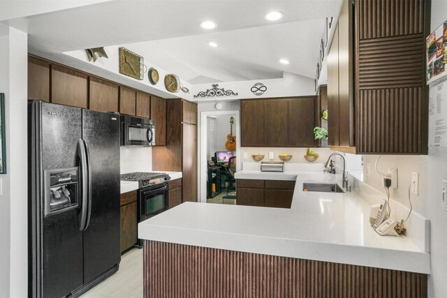 kitchen featuring a peninsula, a sink, vaulted ceiling, dark brown cabinets, and black appliances