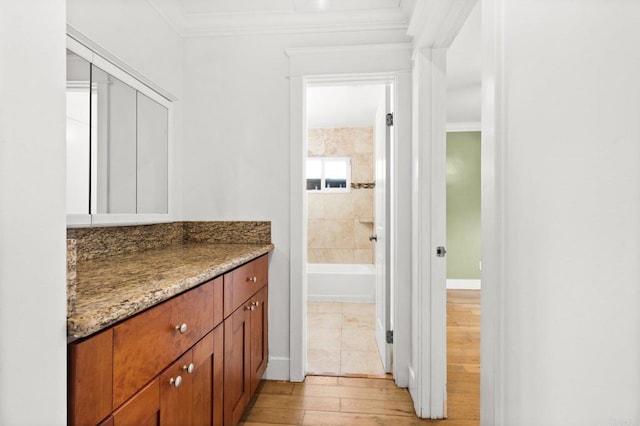 full bathroom featuring vanity, wood finished floors, baseboards, crown molding, and a bath