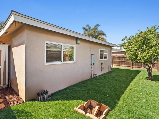 rear view of property featuring stucco siding, a lawn, and fence