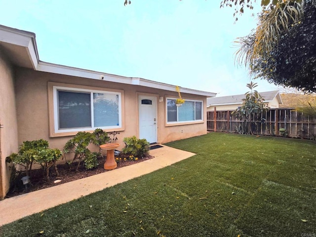 view of front of home with stucco siding, a front lawn, and fence