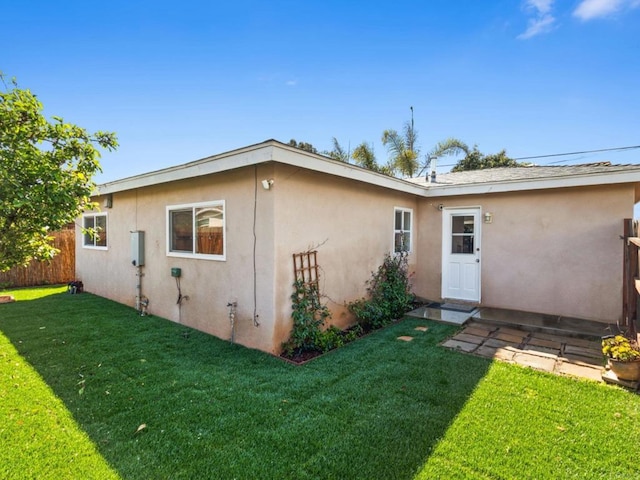 rear view of property with stucco siding, a lawn, and fence