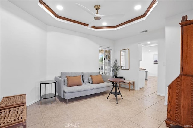 living area featuring ceiling fan, visible vents, baseboards, a tray ceiling, and crown molding