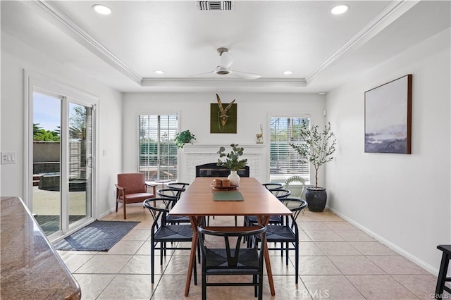 dining space with light tile patterned floors, a tray ceiling, a fireplace, and crown molding