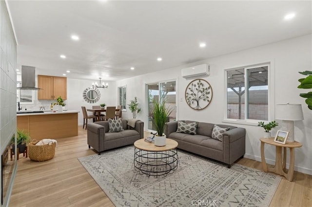 living area with a wall unit AC, a notable chandelier, recessed lighting, light wood-style floors, and baseboards