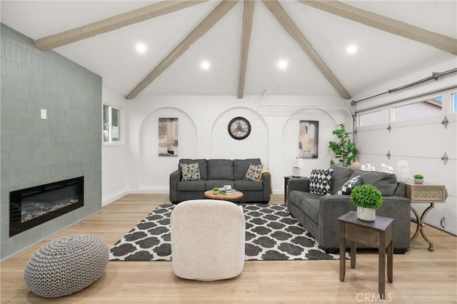 living area featuring high vaulted ceiling, wood finished floors, a garage, a tile fireplace, and beamed ceiling