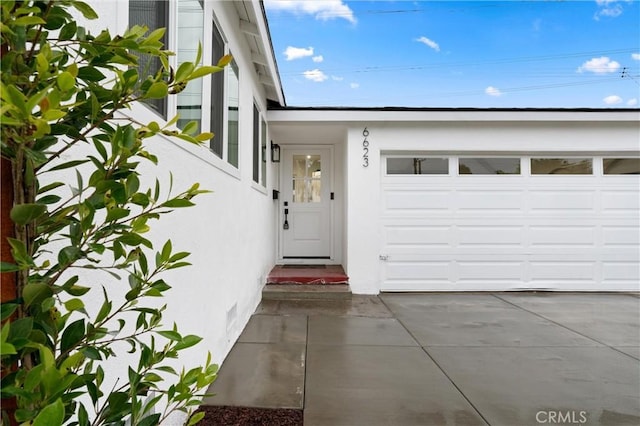 entrance to property featuring driveway, an attached garage, and stucco siding