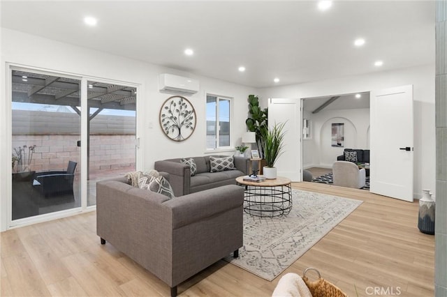 living area featuring recessed lighting, light wood-style flooring, arched walkways, and a wall mounted AC