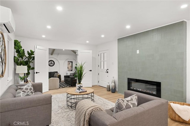 living room featuring light wood-type flooring, recessed lighting, a tiled fireplace, and a wall mounted air conditioner