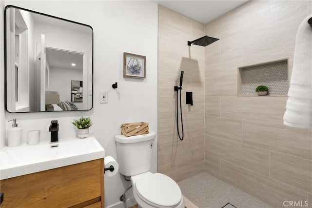 bathroom featuring toilet, a tile shower, and vanity