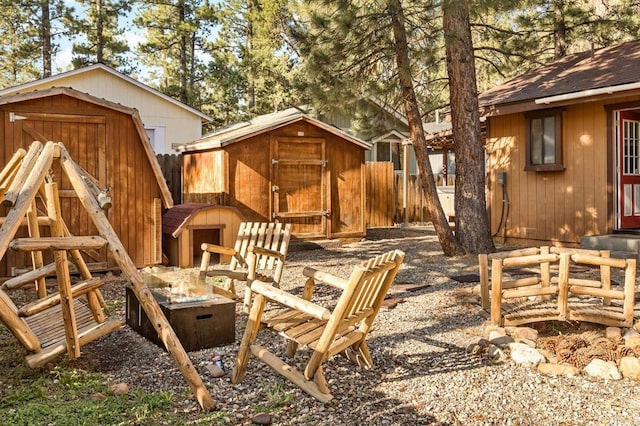 view of playground featuring a storage shed, fence, and an outbuilding