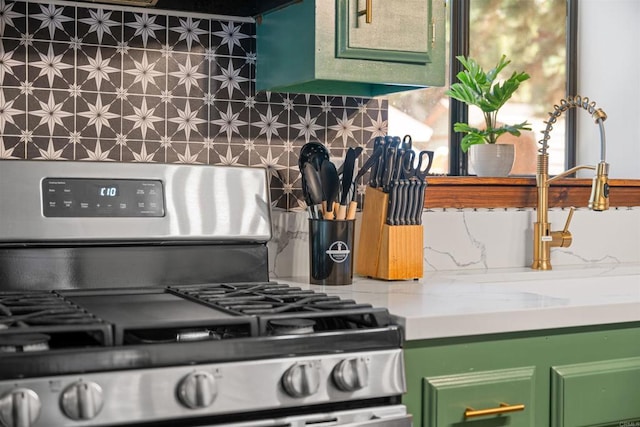 kitchen with backsplash, green cabinets, stainless steel range with gas stovetop, and light countertops