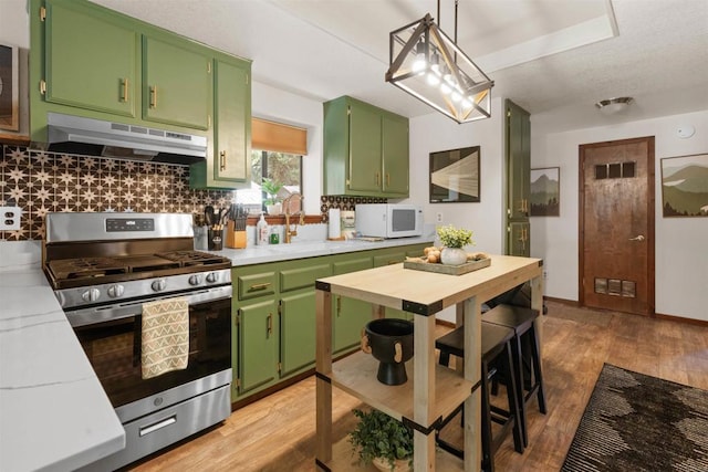 kitchen featuring white microwave, under cabinet range hood, green cabinets, stainless steel gas range, and decorative backsplash