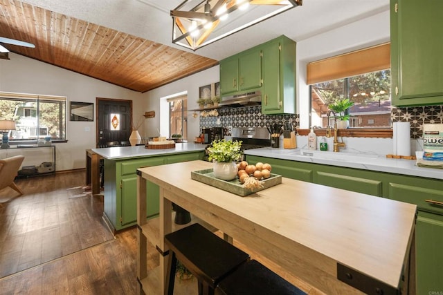 kitchen featuring under cabinet range hood, green cabinets, vaulted ceiling, tasteful backsplash, and stainless steel range