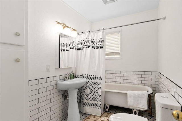 full bathroom with toilet, a tub, tile walls, and wainscoting